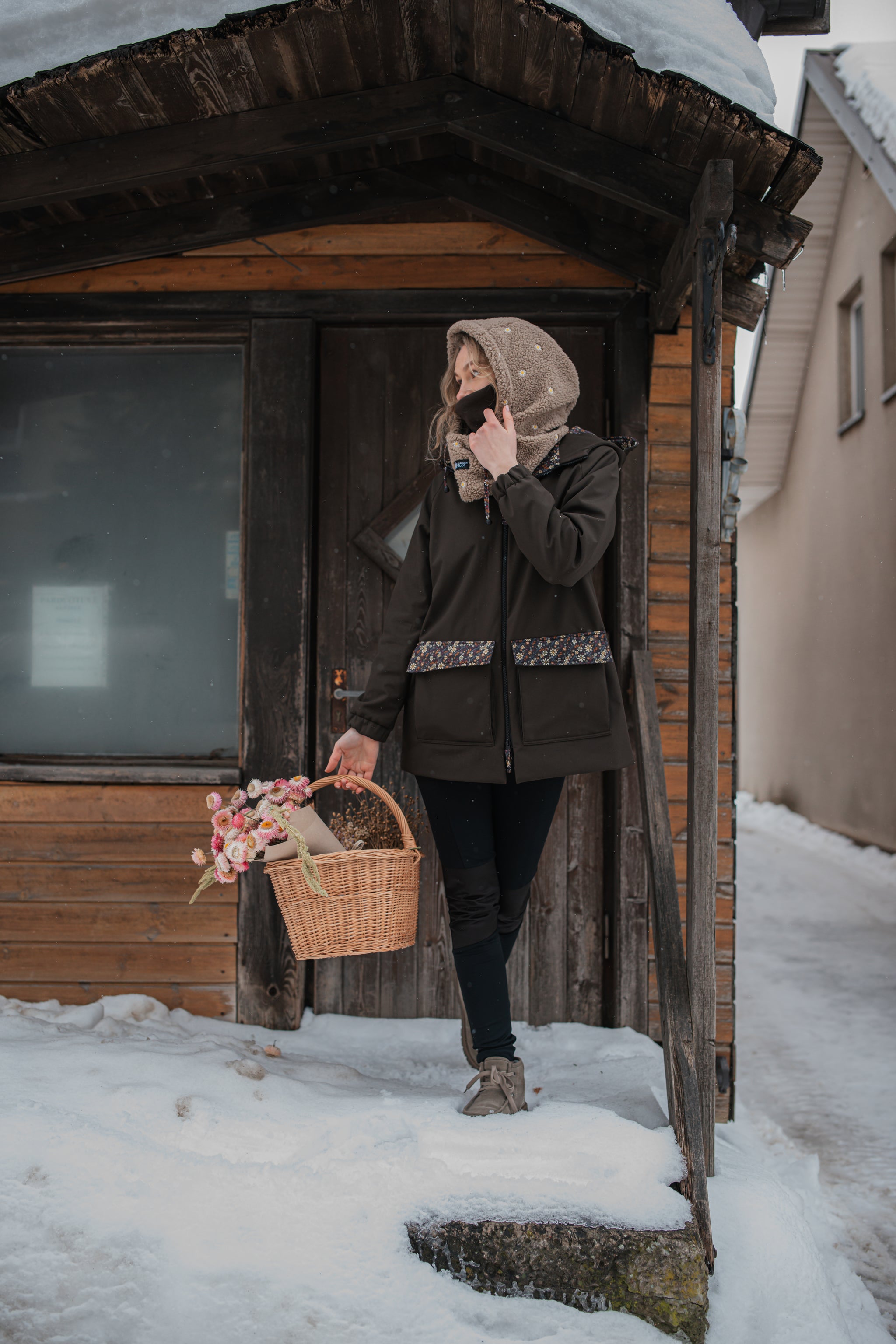 Moteris su ruda gėlėta sodo striuke žiemą — kalba telefonu ir laiko gėlių krepšelį
